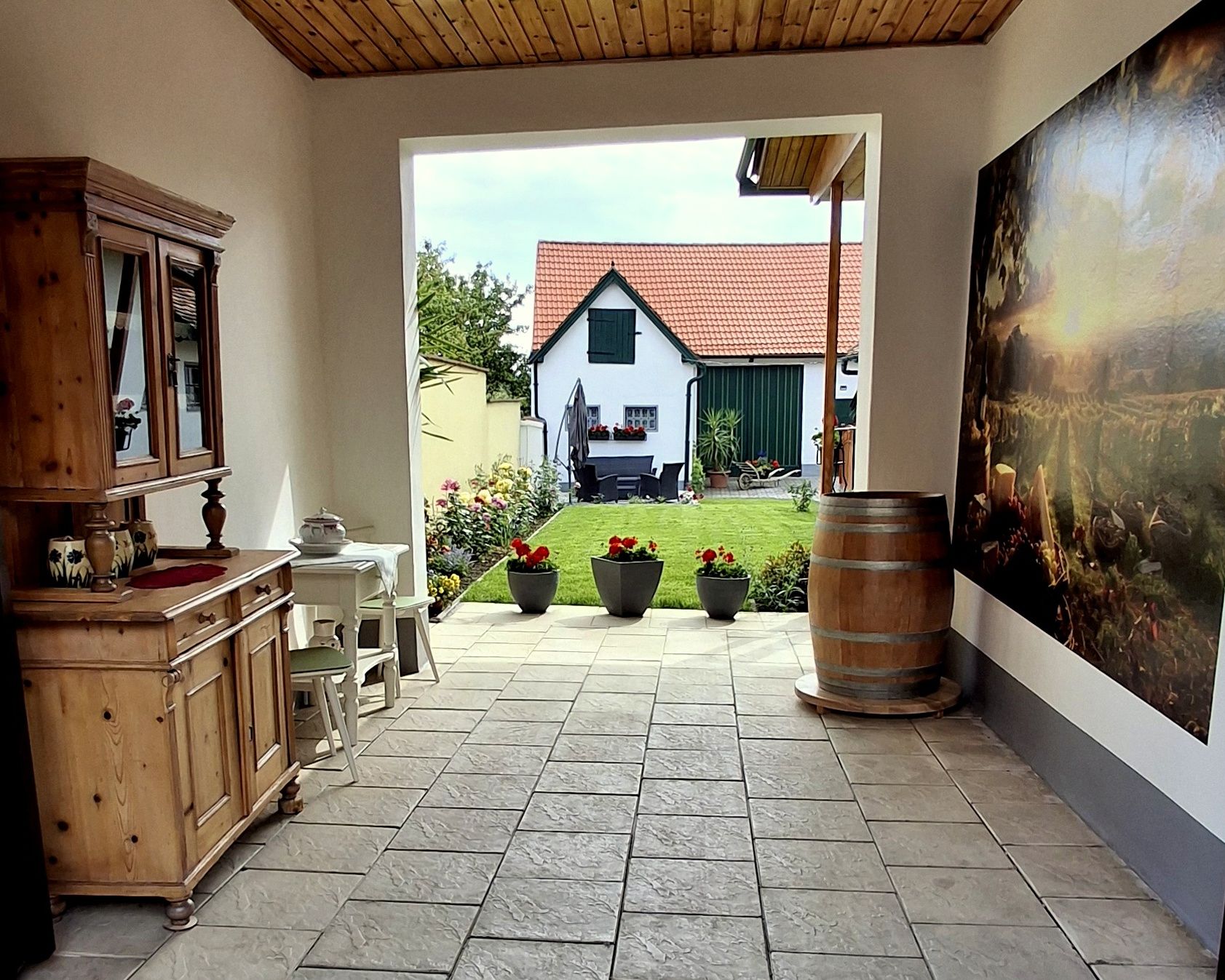 Inner courtyard with wooden furniture, plants and a view of a house with a red roof.
