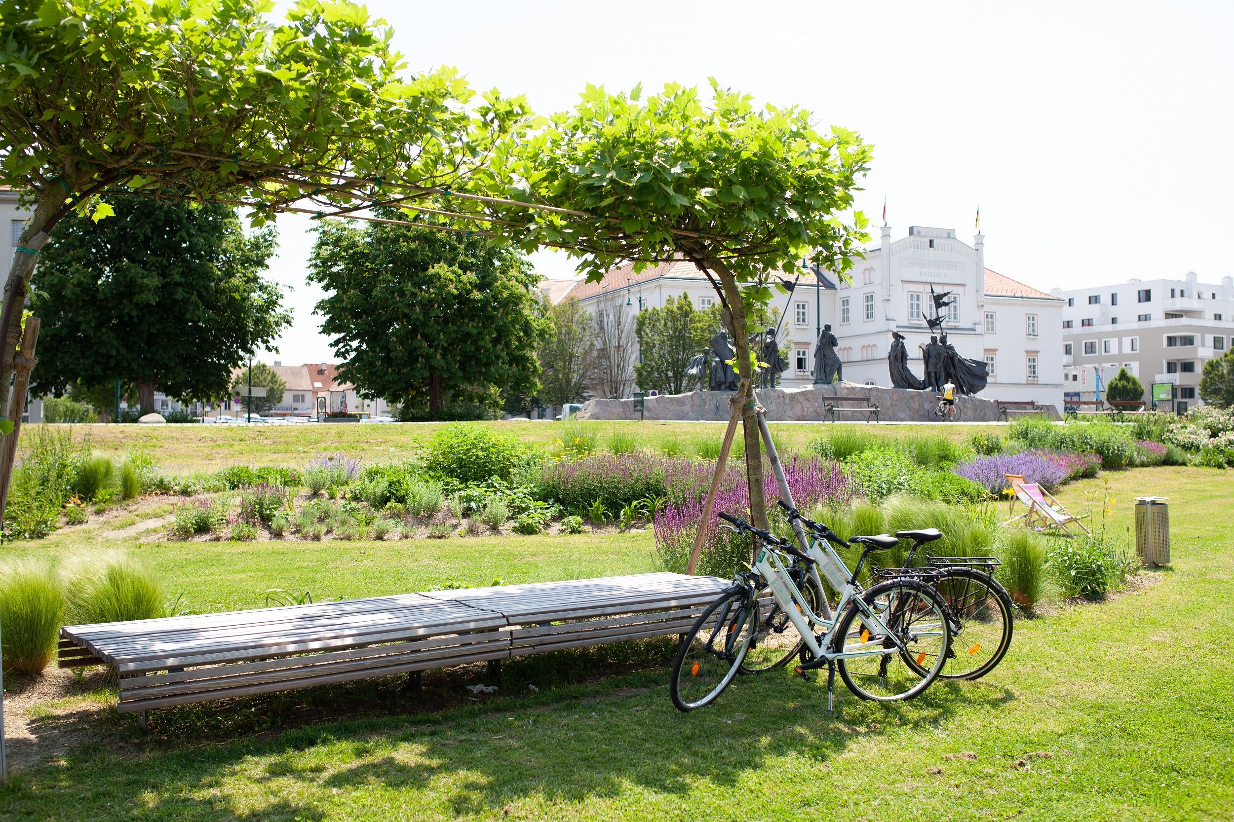 Two bicycles are parked on the green banks of the Danube, with the town hall visible in the background 