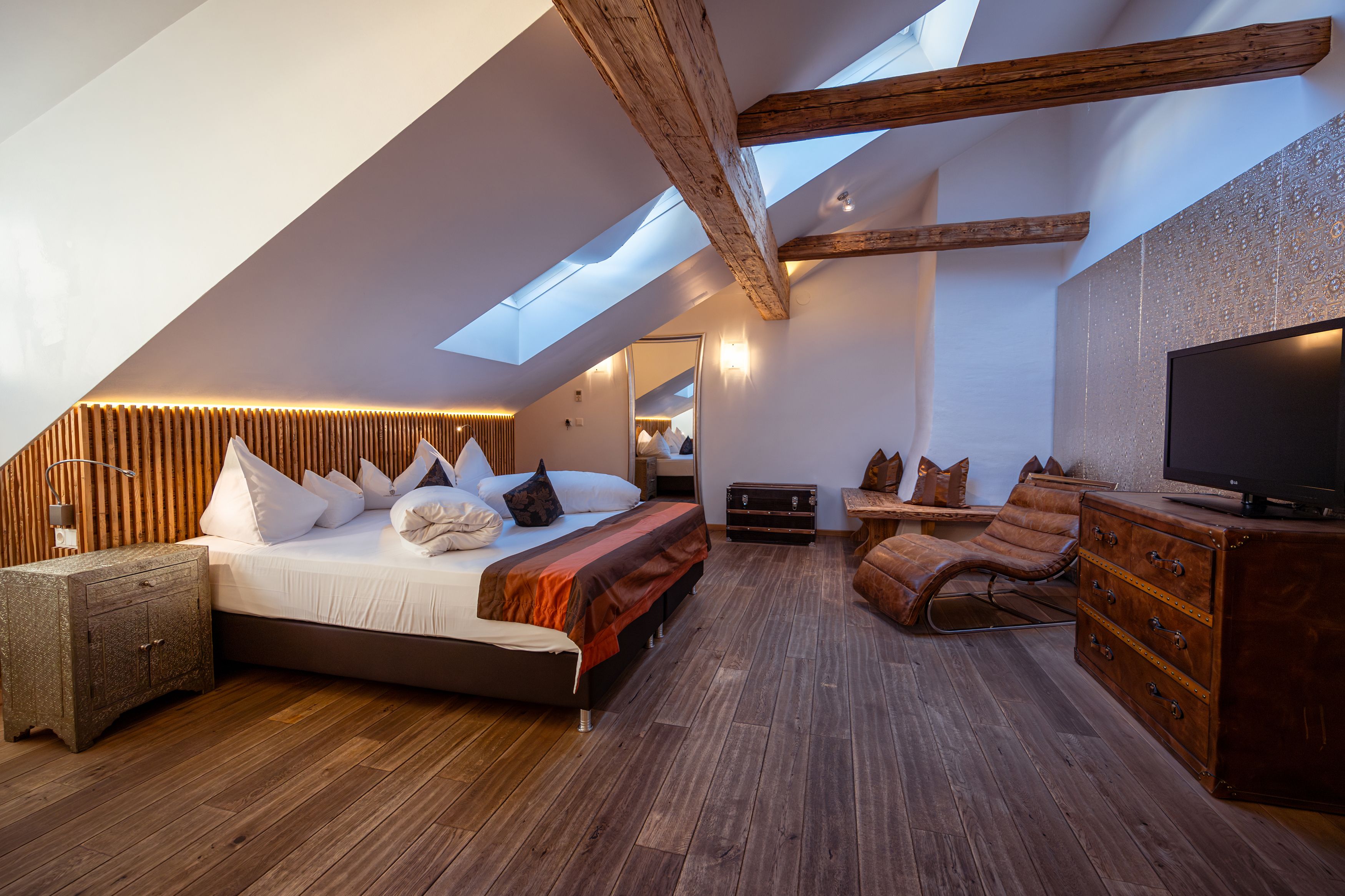 Cozy hotel room with wooden beams, skylights, large bed and leather armchair.