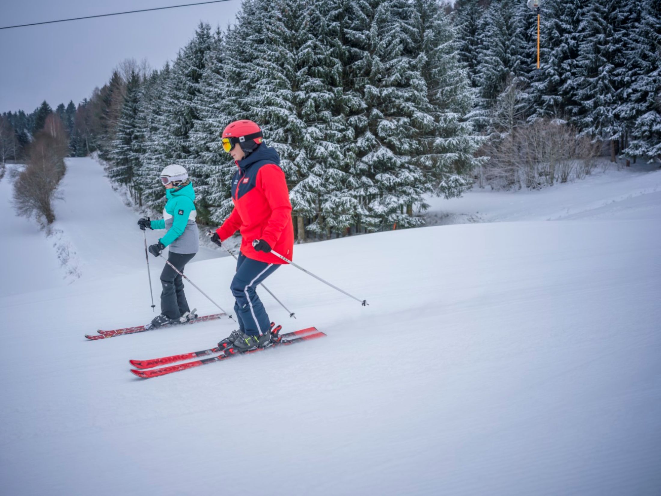 Two skiers on a snowy slope, surrounded by snow-covered trees.
