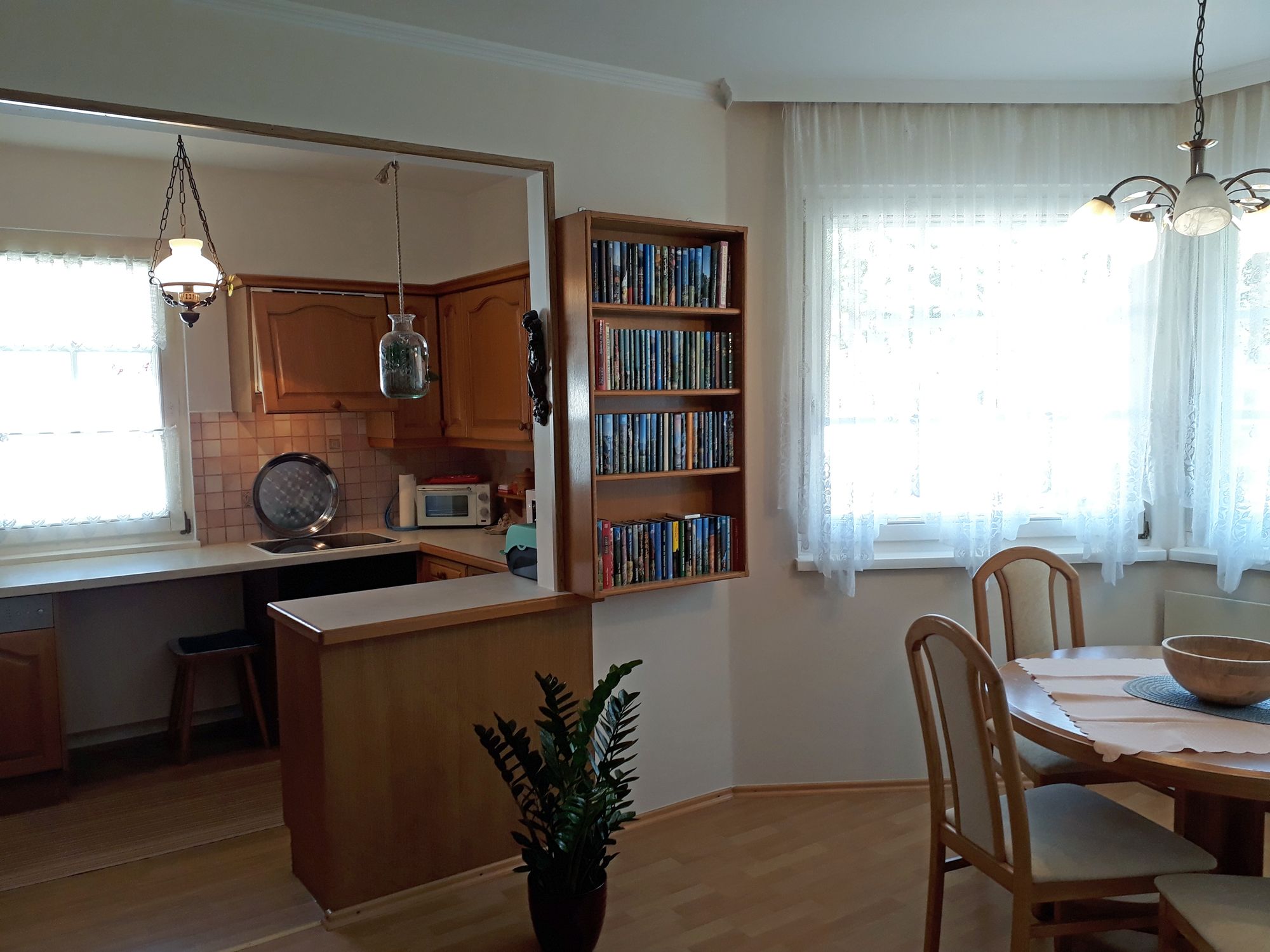 Cozy kitchen with wooden furniture, dining table and bookshelf.
