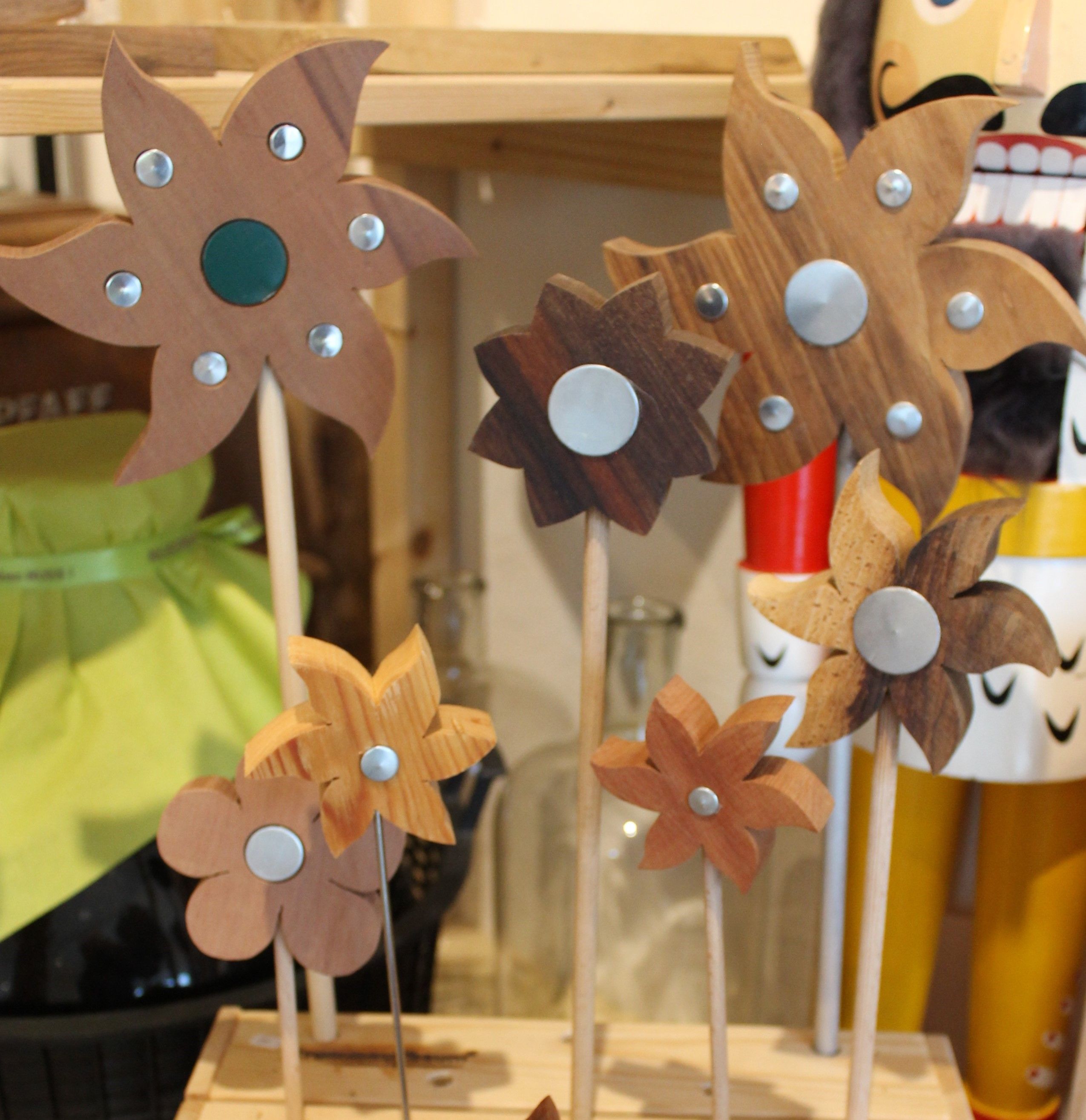 Wooden flowers with metal decorations on rods on a shelf.