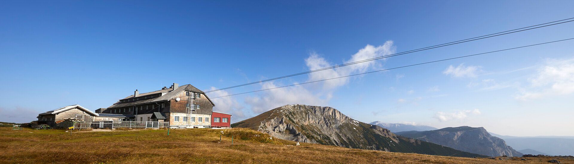 Panoramic view of a mountain hut with surrounding peaks under a blue sky.