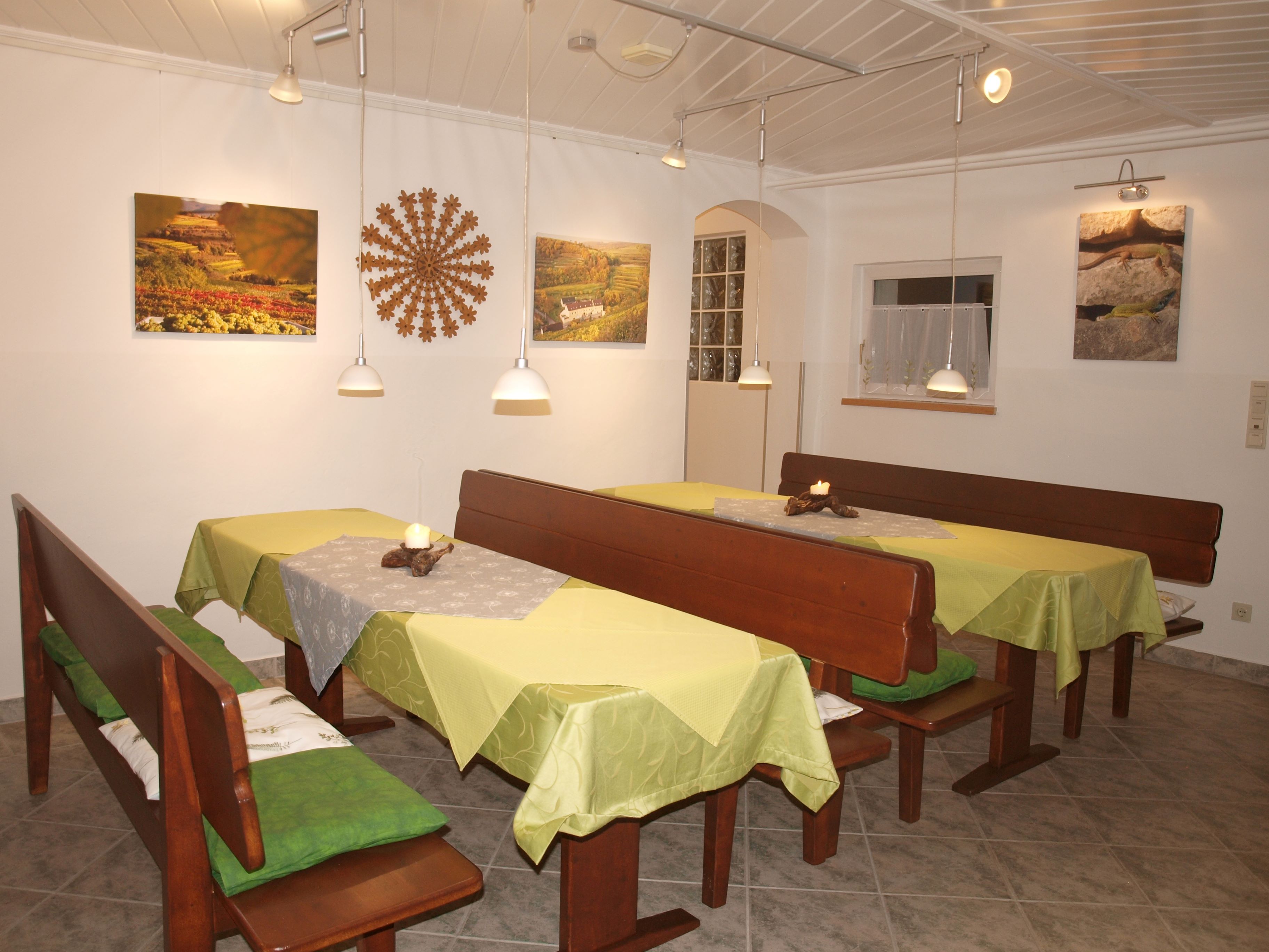 A cozy breakfast room with wooden benches, green tablecloths and wall decorations.