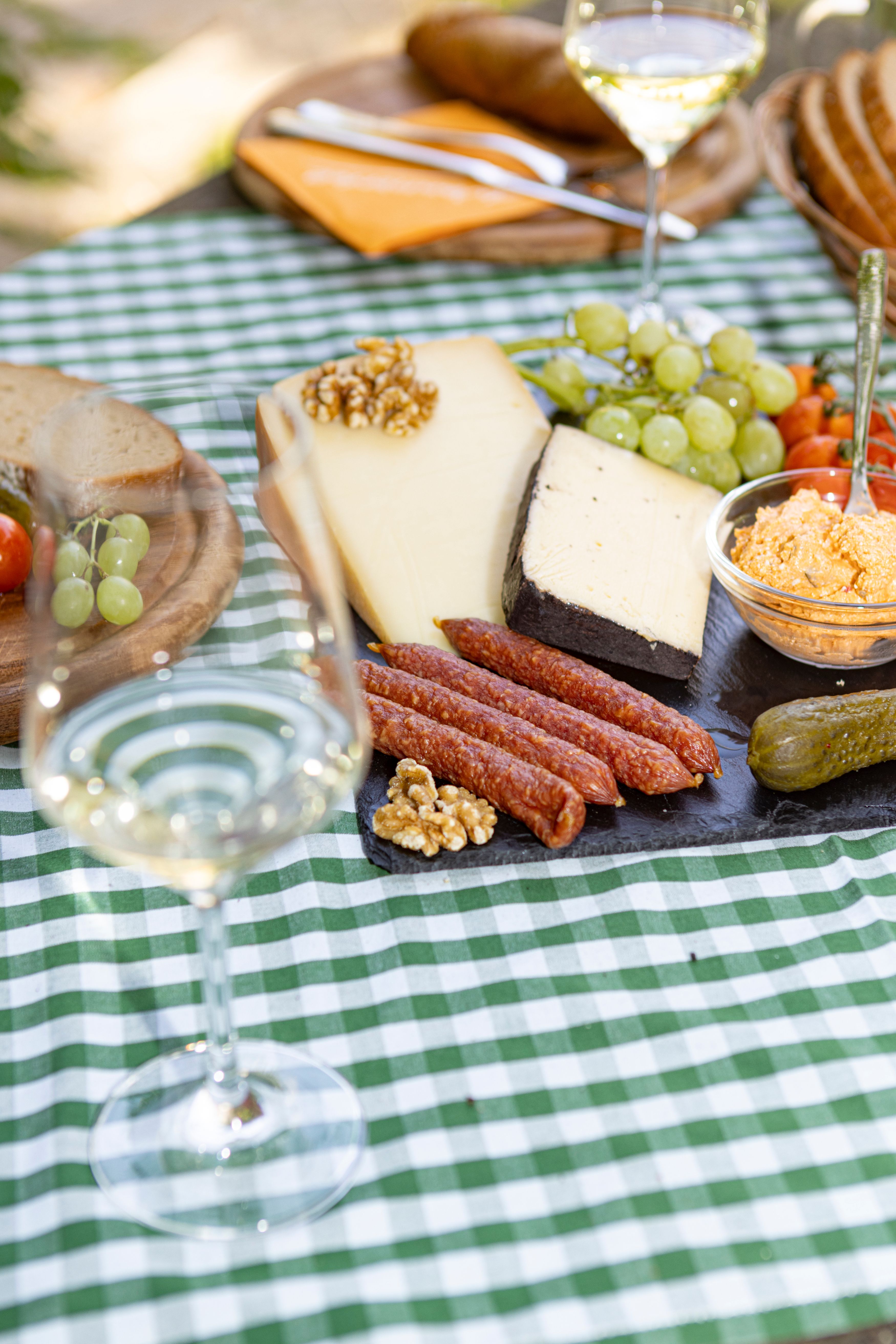 Picnic table with cheese, sausage, bread, grapes and a glass of white wine.