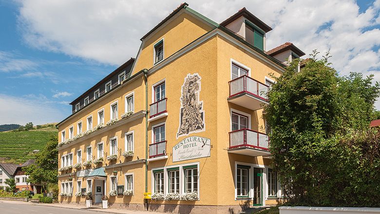 Yellow hotel building with balconies and plants, blue sky in the background.