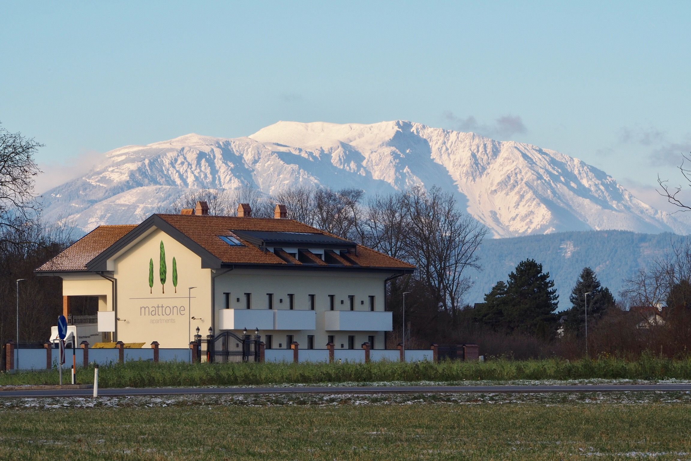 Building with the inscription 'mattone apartments' in front of a snow-covered mountain in the background.