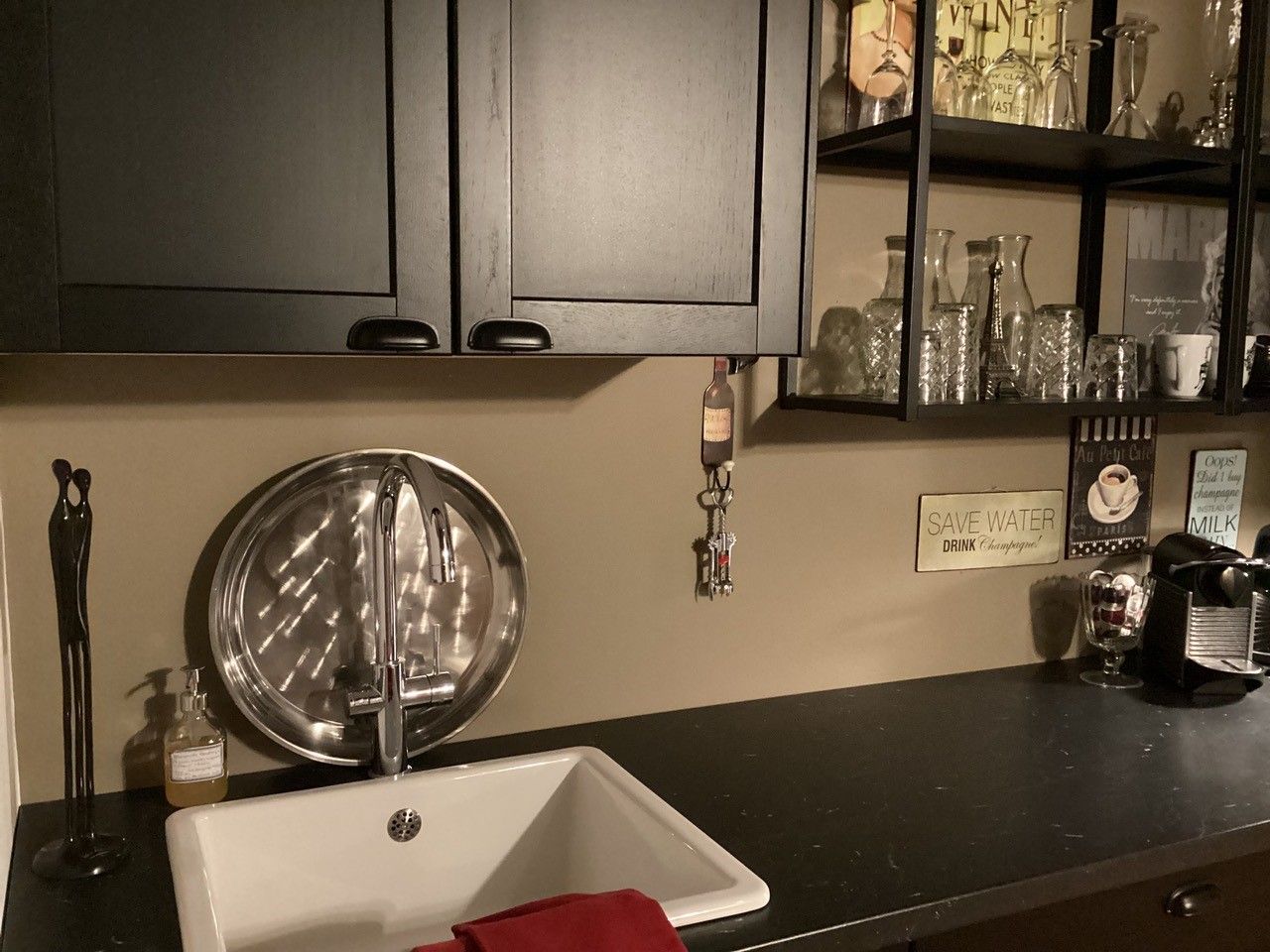 Modern kitchenette with sink, black cupboard, shelves with glasses and coffee machine.