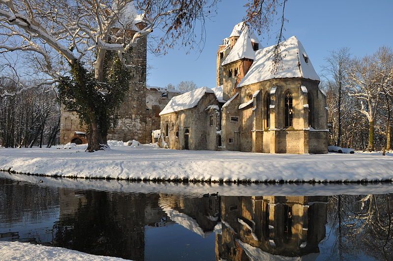 Pottendorf castle ruins in winter with snow and reflection in the water.