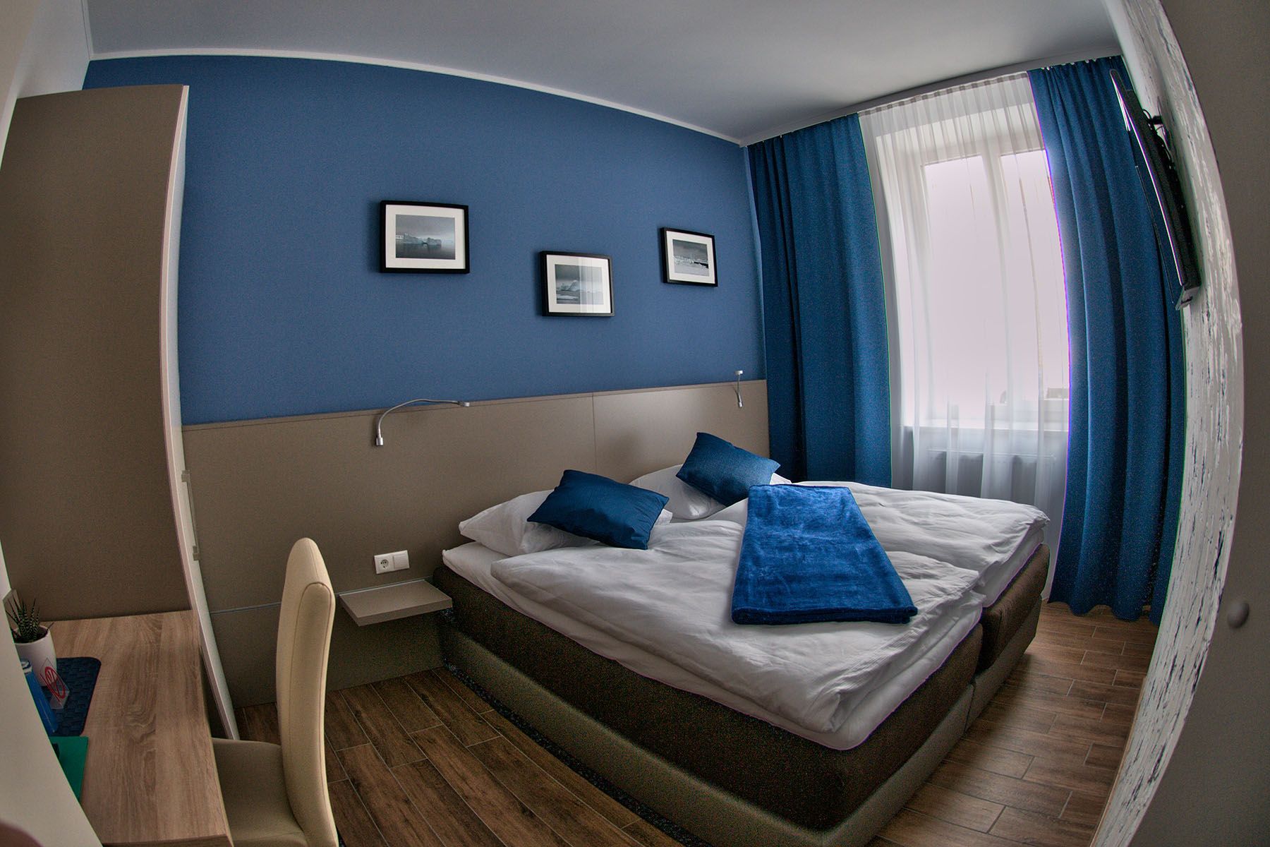 Modern guest room with blue accent, double bed and desk.