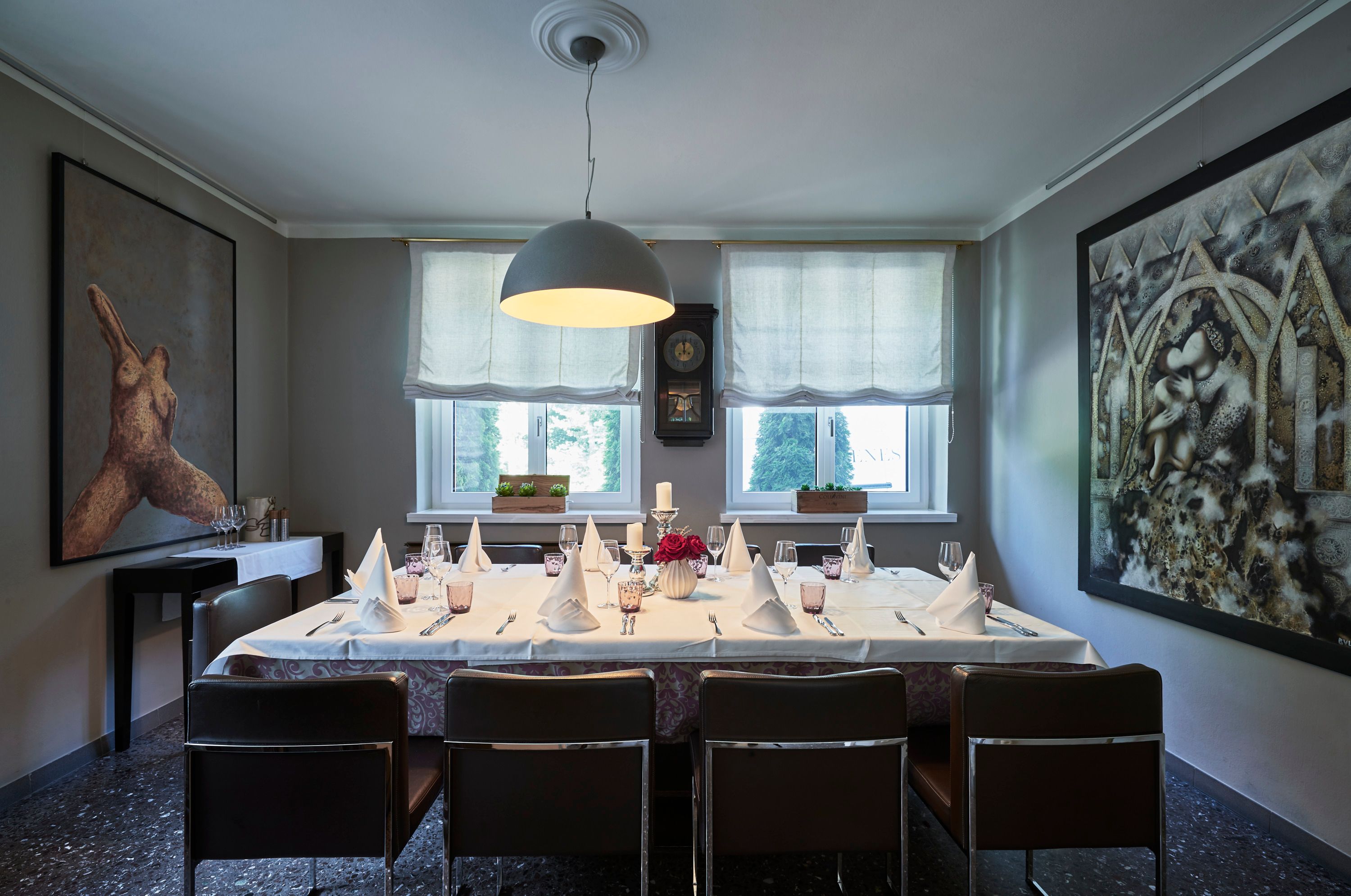 Elegant dining room with table setting, works of art on the walls and large windows.