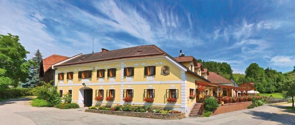 Traditional inn with yellow façade, surrounded by green landscape and blue sky.