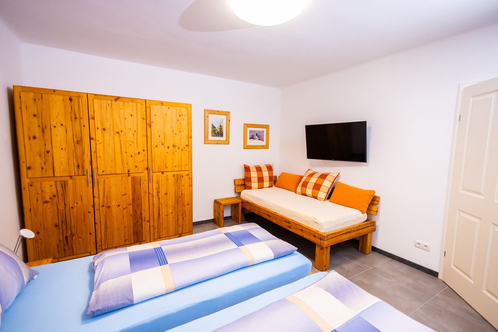 Bedroom with wooden furniture, two beds, sofa, TV and pictures on the wall.