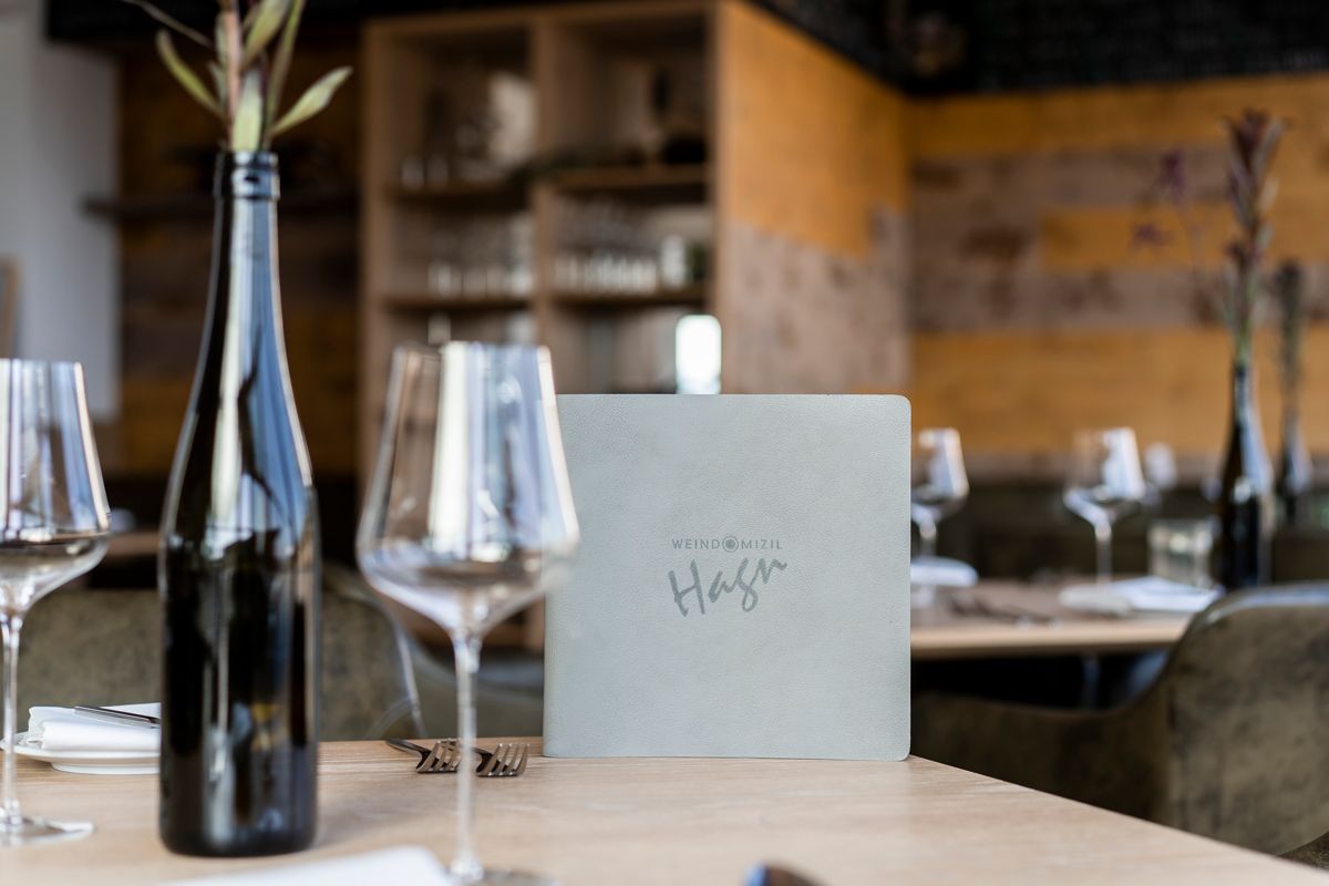 A set table in a restaurant with wine glasses, a bottle of wine and a menu.