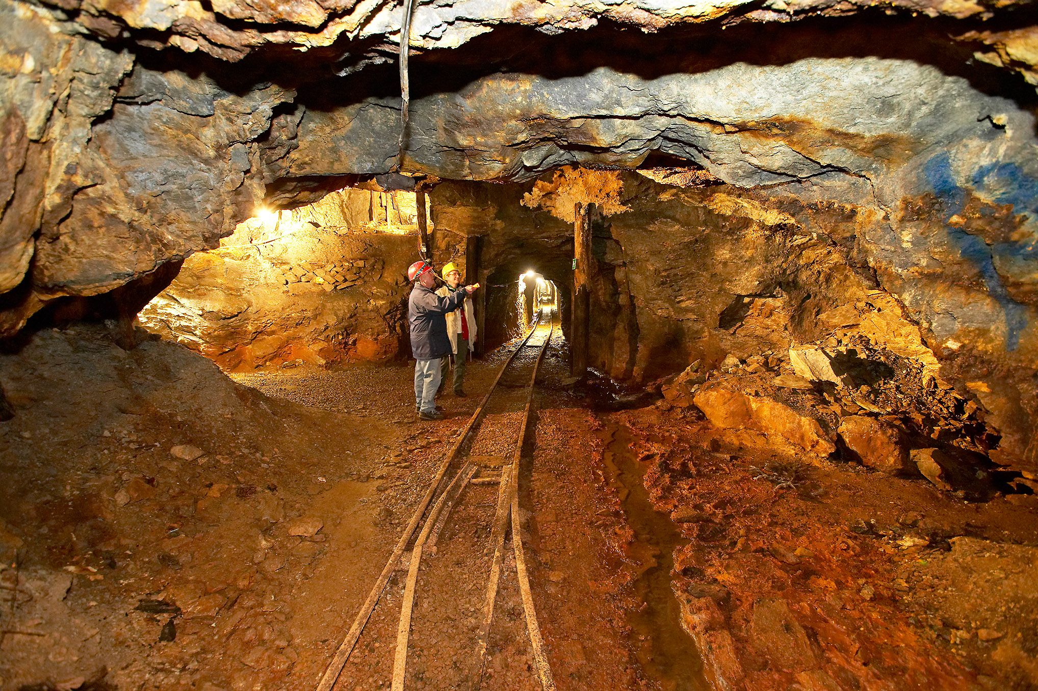 Interior view of an illuminated mine tunnel with two people in hard hats.