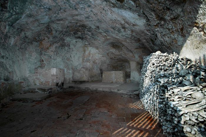 Interior view of a cave church with a pile of bones on the wall.