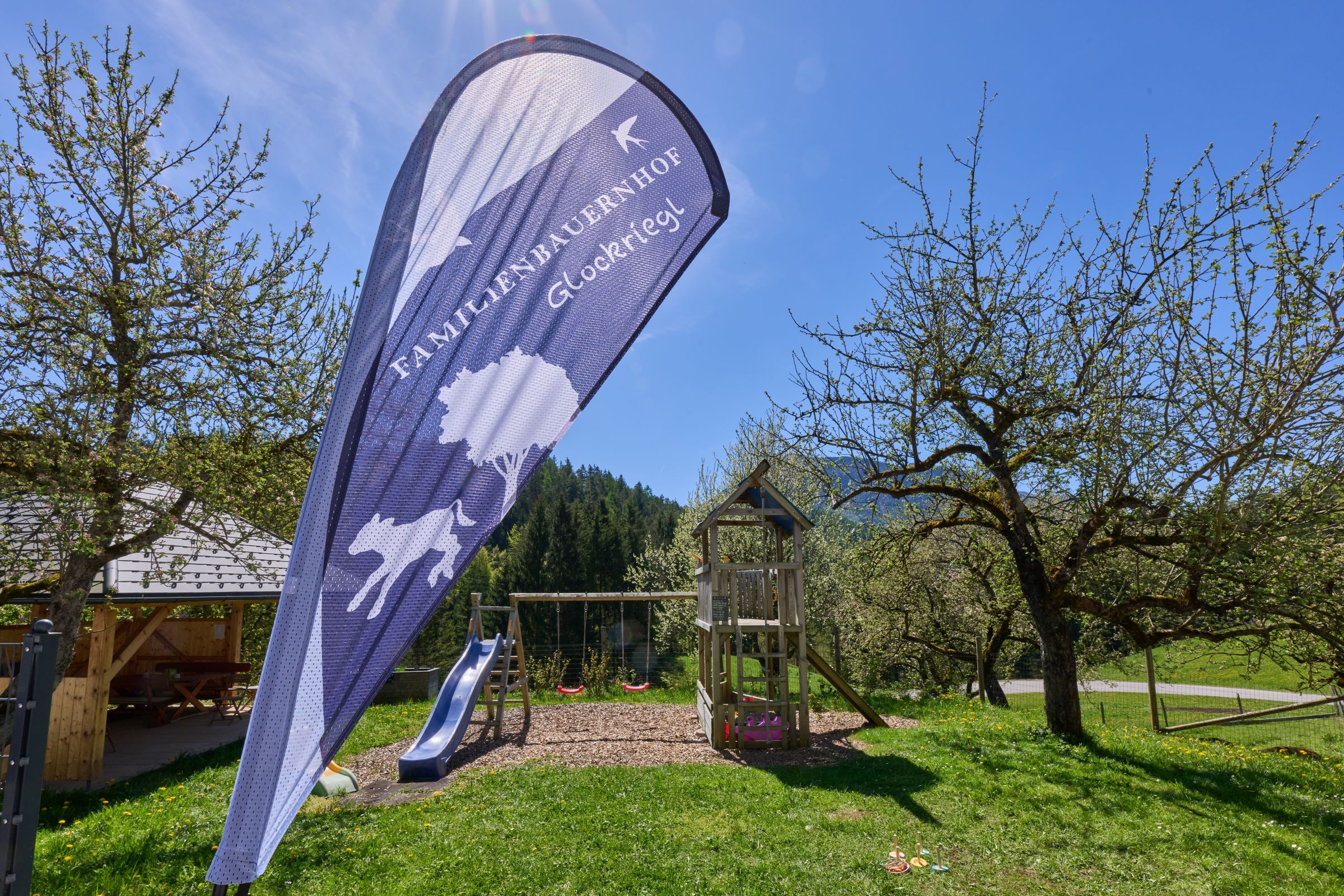 Playground with slide and swing in the garden of a farm, surrounded by trees and meadows.