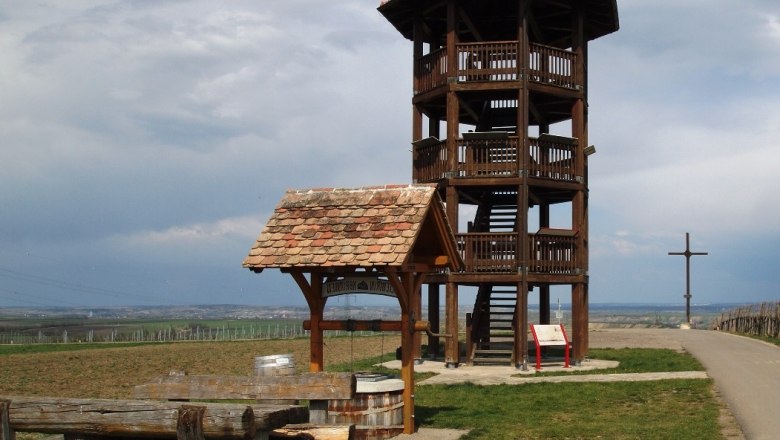 Wooden observation tower on a meadow with benches and a cross in the background.
