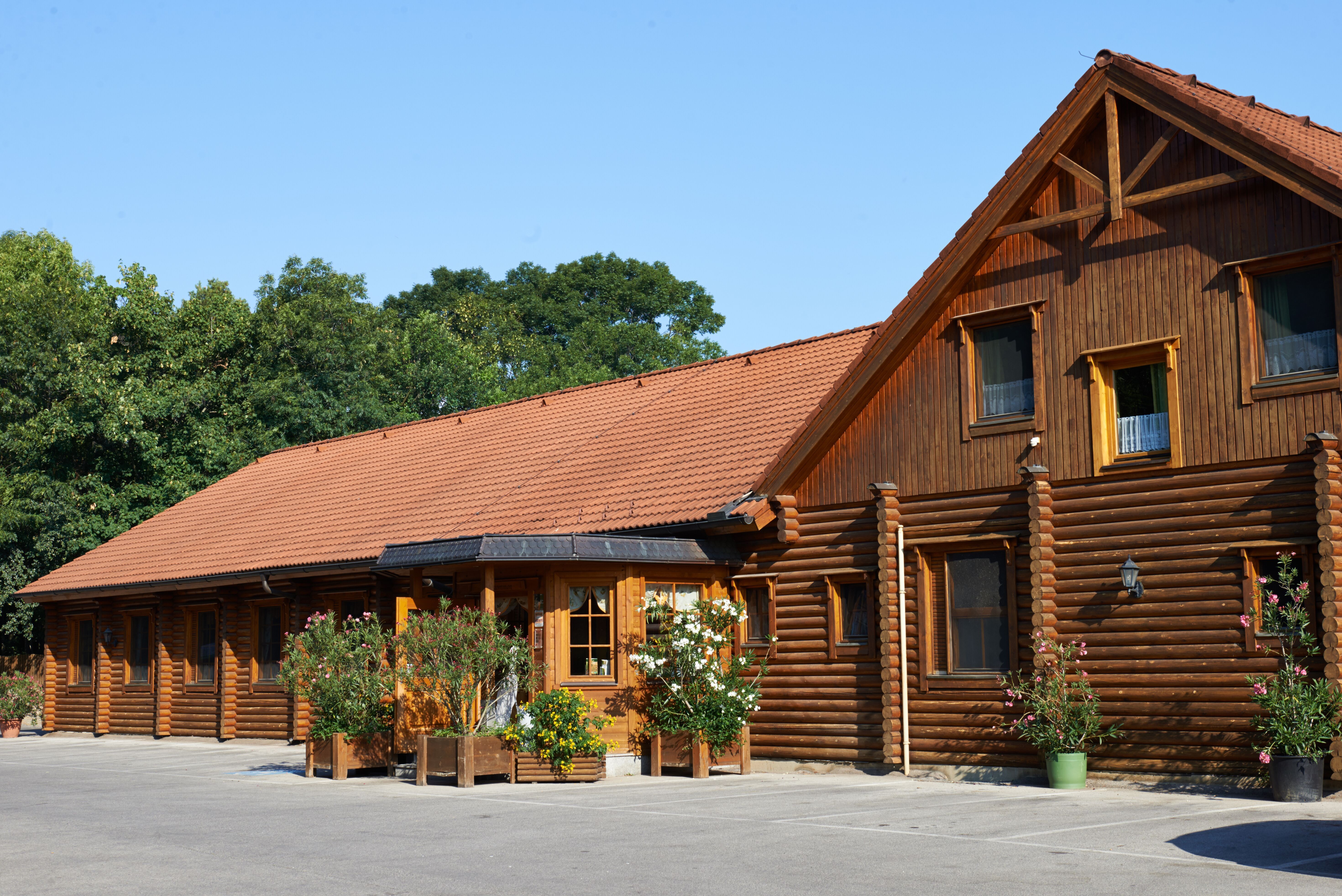 Log cabin with red tiled roof and plants in front of it.