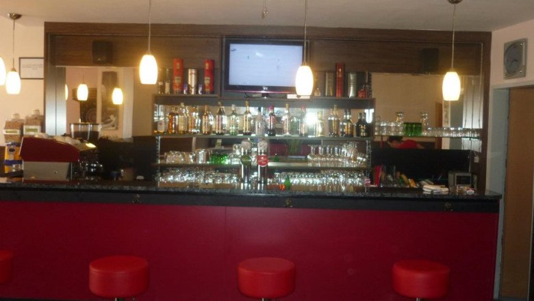 Interior view of a bar with red stools and illuminated shelves full of bottles.