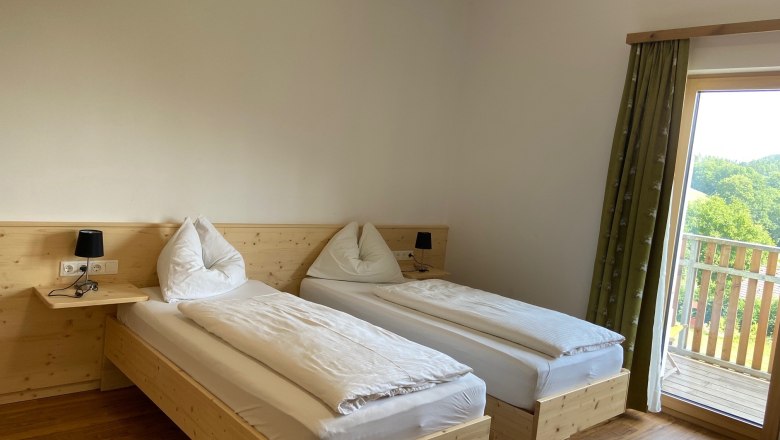 Double room with wooden floor, two single beds, bedside lamps and a balcony with a view of the countryside.