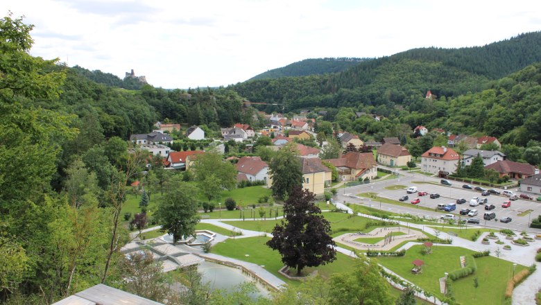View from a viewing platform of a town with surrounding woods and a ruined castle in the background.
