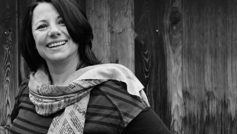 Black and white photo of a smiling woman with a scarf in front of a wooden wall.
