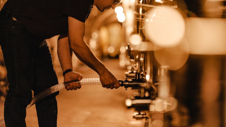 Person works in a wine cellar with tanks.