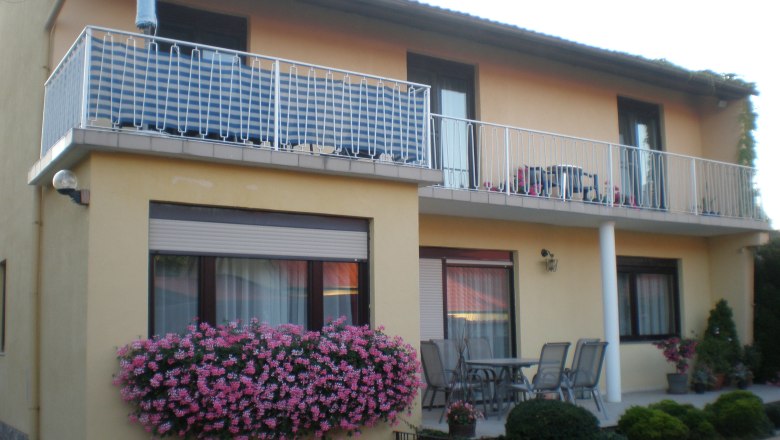 Two-storey house with balcony, flowers and garden furniture.