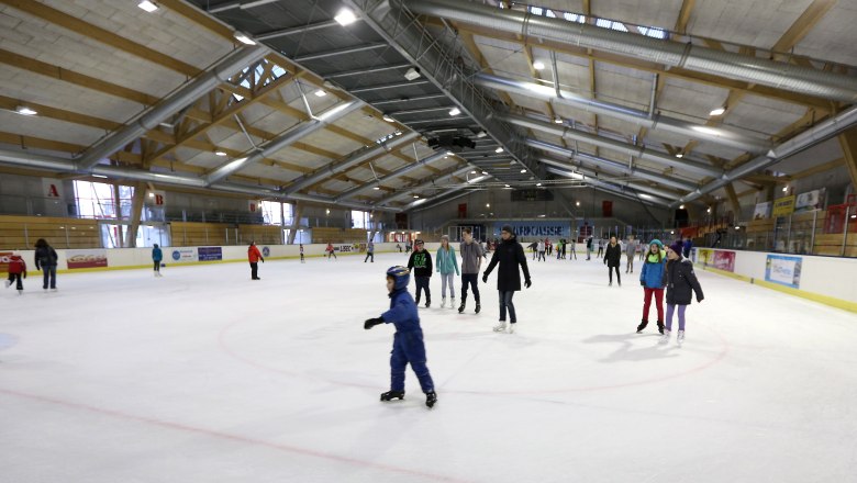 People ice skating in a large ice rink.