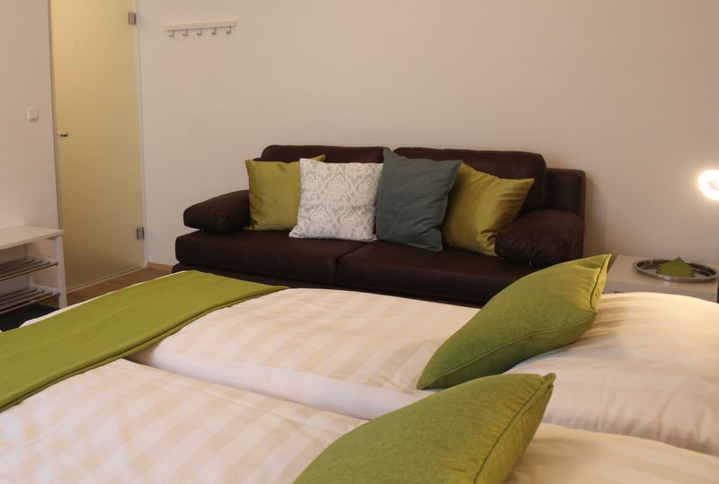 A cozy room with a double bed and a brown couch, decorated with green and white cushions.