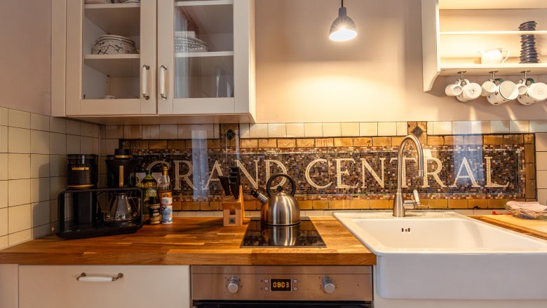 Kitchen with wooden counters, sink, stove and mosaic tiles with 'GRAND CENTRAL'.