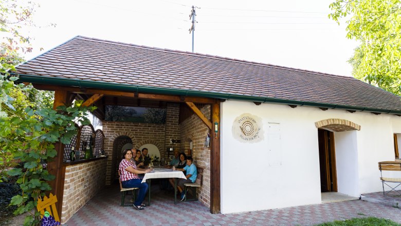 A family is sitting at a table in a covered outdoor area of a building with the sign 'Tankstation Selbstservice'.