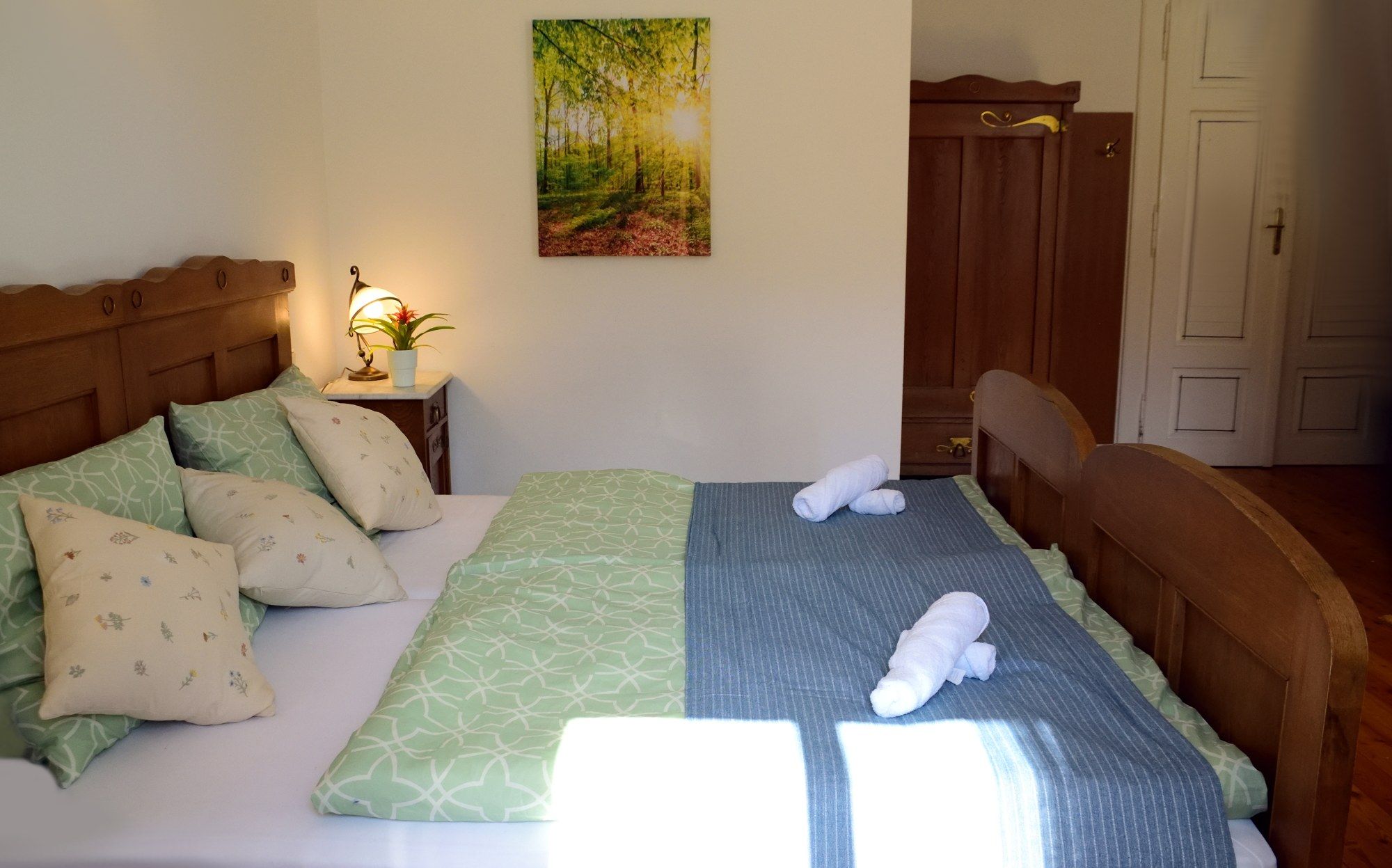 Cozy double room with wooden furniture, green bedding and a picture on the wall.