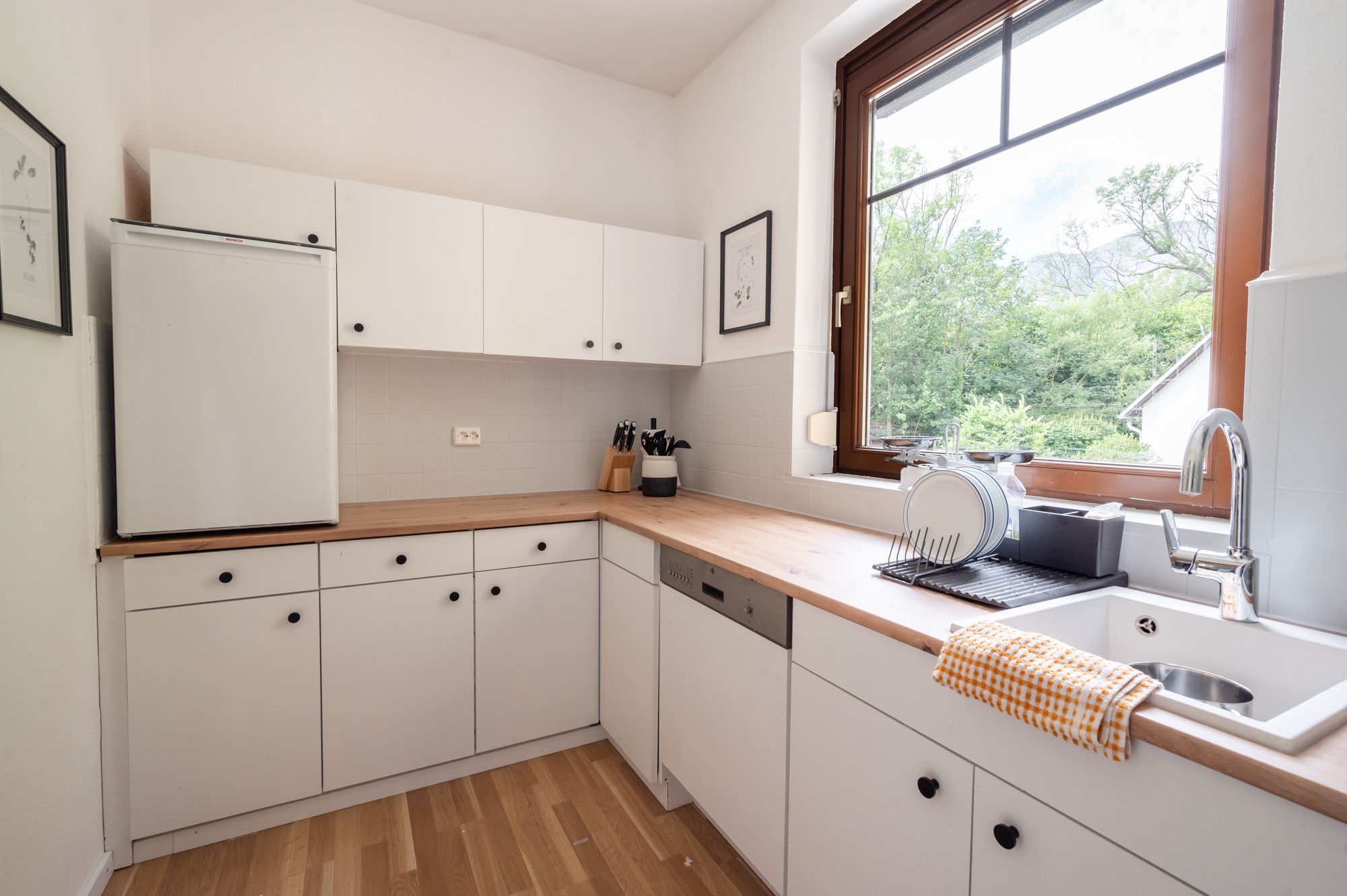 Modern kitchen with white cupboards, wooden worktop and large window with a view of the greenery.
