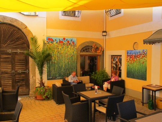 A cozy inner courtyard of a café with yellow walls, plants and paintings. Two people are sitting at a table.
