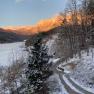 Snow-covered landscape with mountains in the background, illuminated by the evening sun.