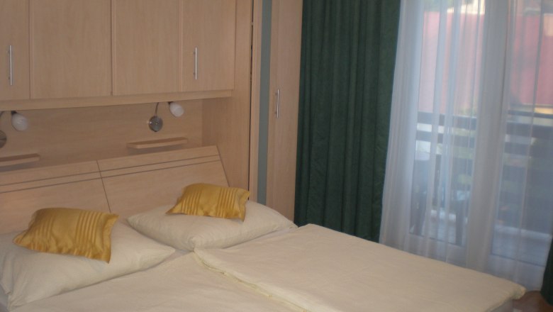 A bedroom with a double bed, yellow cushions, wooden wardrobes and a window with green curtains.