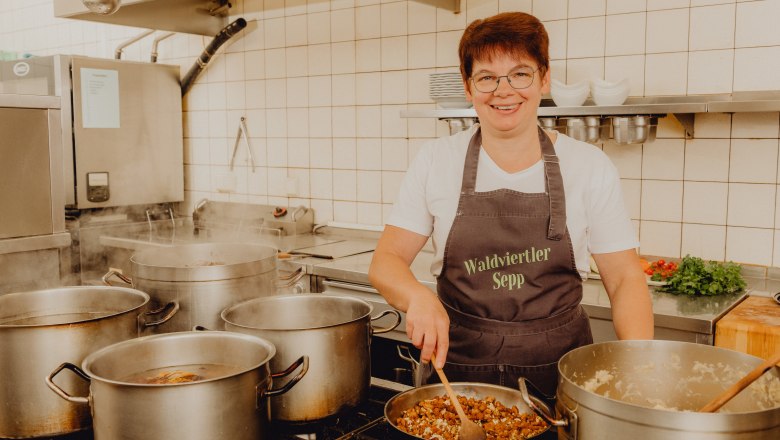 A cook in a professional kitchen serving several pots on a stove.