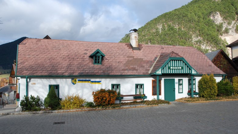 Schneeberg Museum Puchberg, a traditional building with a green roof and chimney, surrounded by mountains and trees.