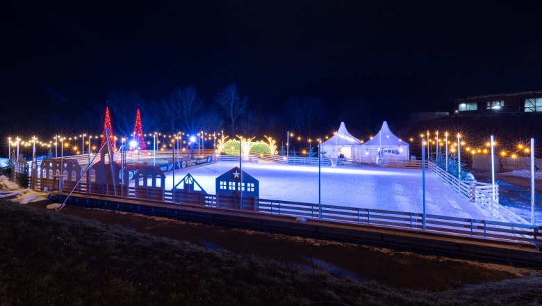 Illuminated ice rink at night with decorative lights and tents.