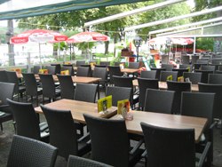 An empty outdoor café with lots of tables and chairs, surrounded by trees.