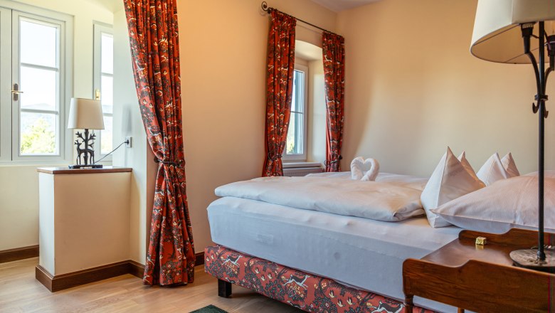 Cozy hotel room with double bed, red curtains and decorative heart-shaped towel.