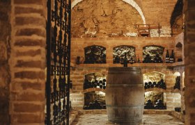 A rustic wine cellar with brick walls, wine racks and a wooden barrel in the middle.
