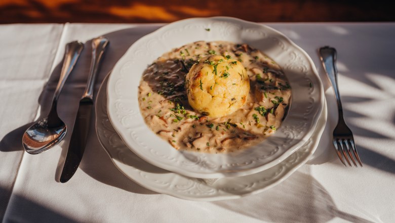 A plate with mushroom sauce and a semolina dumpling, garnished with parsley, on a white tablecloth.