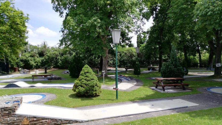 Minigolf course with trees and benches in a park.