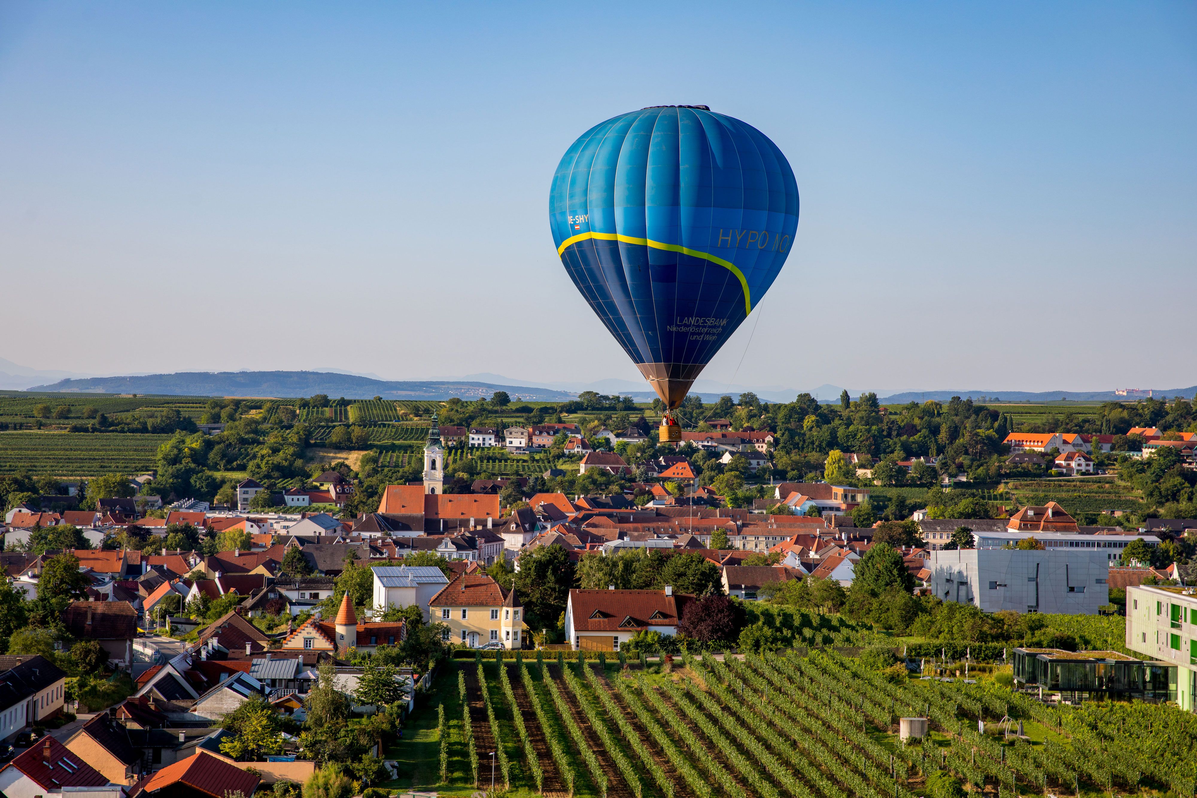 Hot air balloon over a cityscape with vineyards and houses.