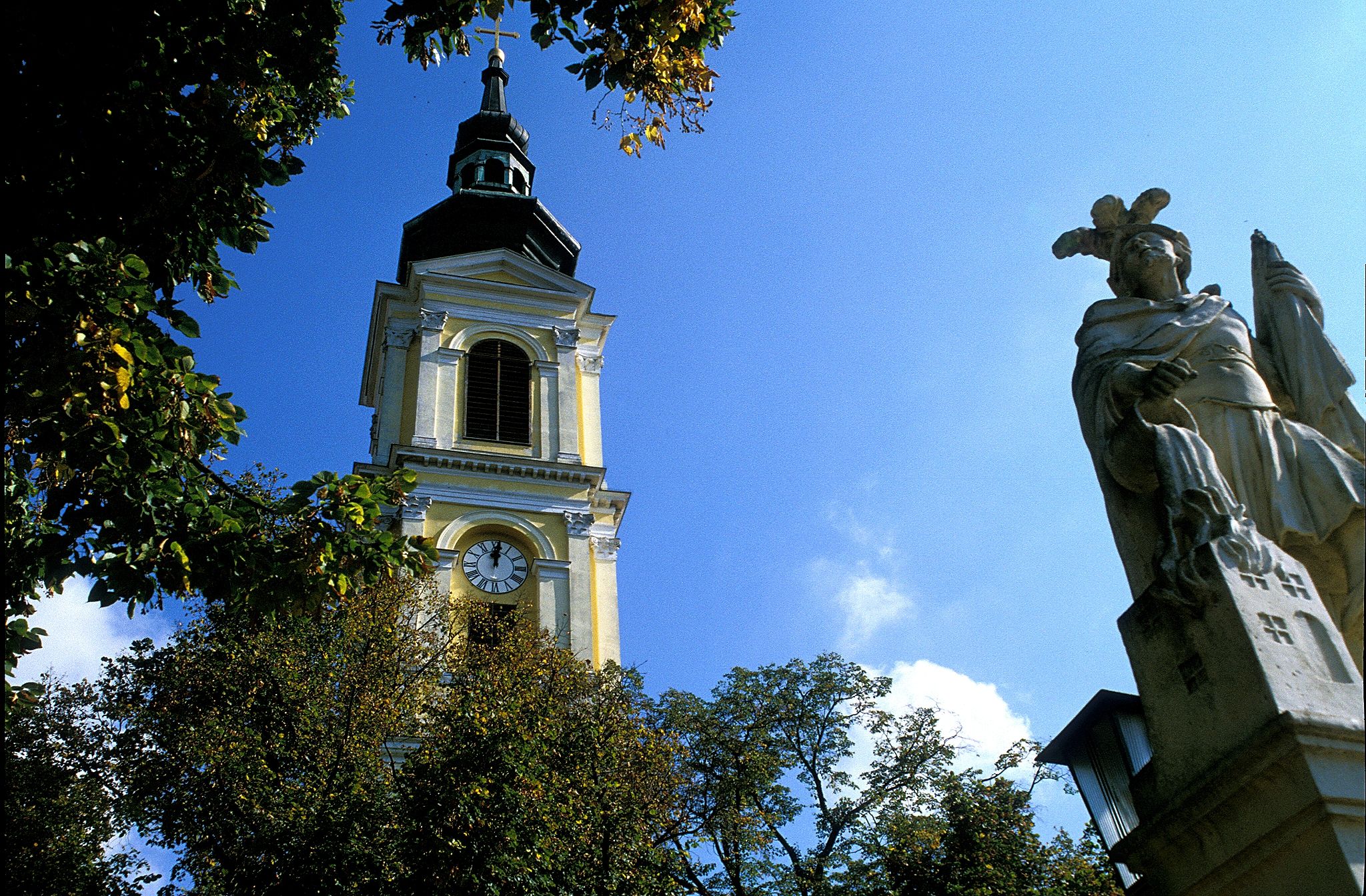 Tower of Großweikersdorf parish church with statue in the foreground.