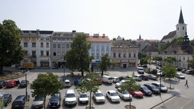 Town square in Hollabrunn with parked cars, historic buildings and a church in the background.