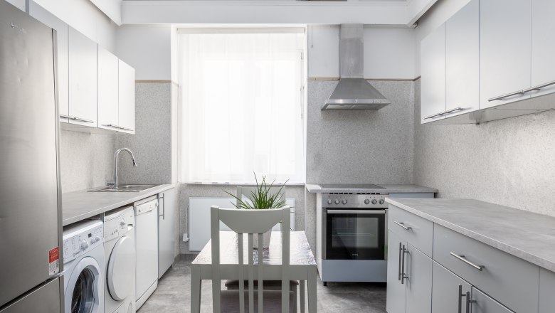 Modern kitchen with washing machine, stove and table with chair.